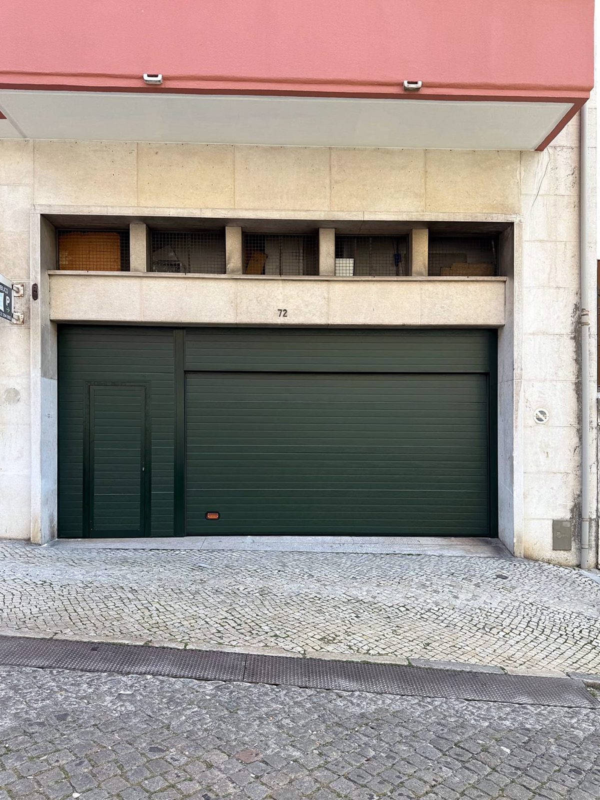 Porta de garagem verde com porta pedonal num edifício